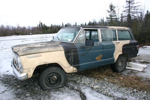 2003 Jeep TJ - A weathered Jeep Wagoneer with a flat tire sits in a snowy, wooded area.