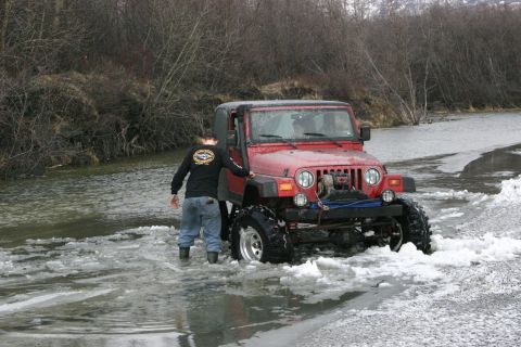 2003 Jeep TJ - A red Jeep Wrangler navigates through a partially frozen body of water with a person standing beside it.