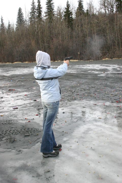 2003 Jeep TJ - A person in a hooded jacket and jeans fires a handgun at an outdoor range, with spent casings scattered on the ground.