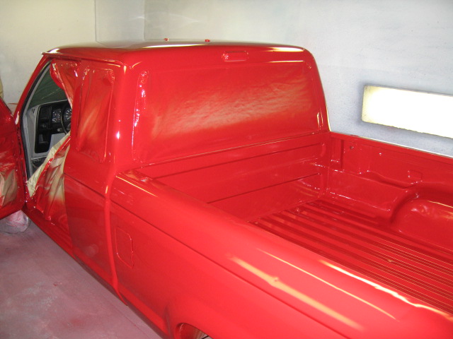 Red Ford Ranger pickup freshly painted in a spray booth, rear three-quarter view with masked interior