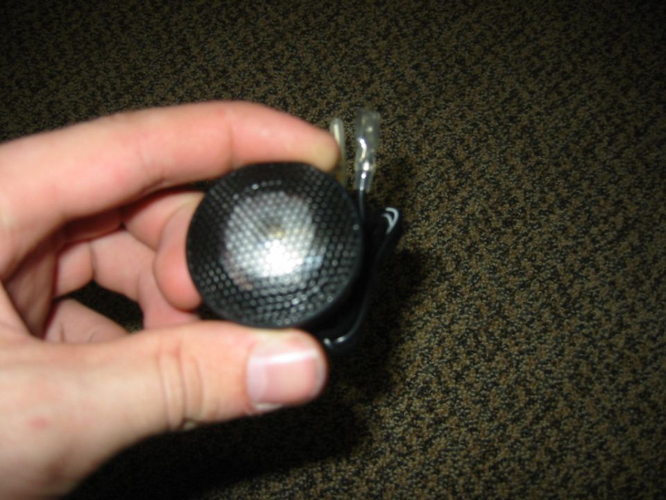 Hand holding a small black car speaker tweeter with wire leads
