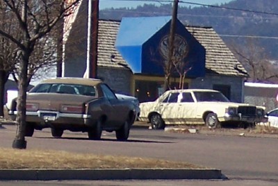 1972 Ford Ranchero - Two cars are parked on a lot in front of a building with a blue awning.