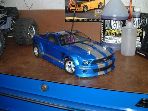 1994 Ford Bronco - A blue remote control car with silver racing stripes sits on a workbench next to a monster truck and bottles of fuel.