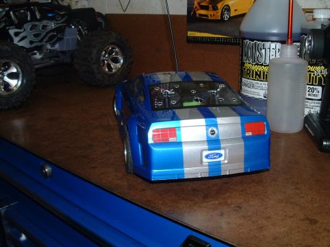 1994 Ford Bronco - A blue and silver striped remote control car is seen from the rear, with other RC vehicles and supplies in the background.