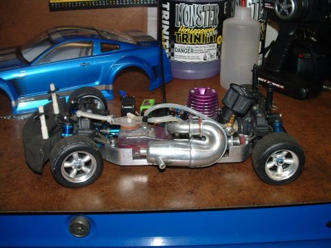 1994 Ford Bronco - A nitro-powered RC car chassis sits on a workbench next to a blue Ford Mustang body shell and a bottle of fuel.
