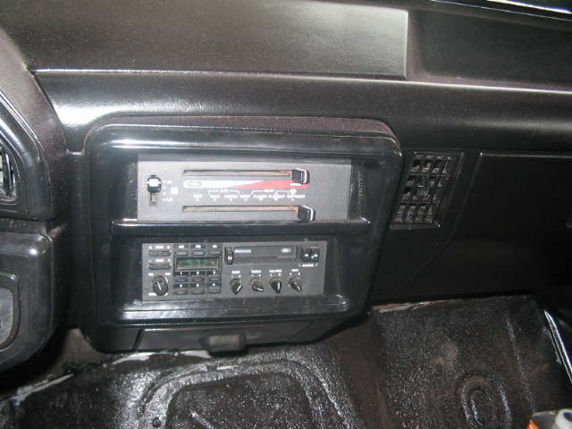 Dashboard of a vehicle showing a dual-DIN radio unit with cassette player above and digital tuner below, plus an air vent