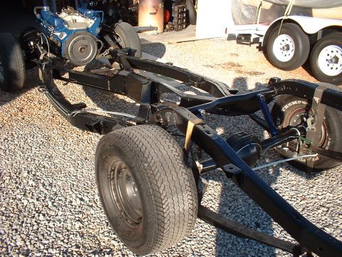 1964 Ford Galaxie - The chassis of a vehicle, including the engine and wheels, is shown outdoors on a gravel surface.