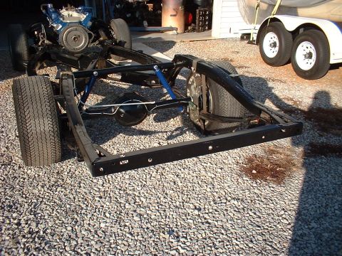 1964 Ford Galaxie - The chassis of a vehicle, including the engine and tires, is shown from a side angle on a gravel surface.