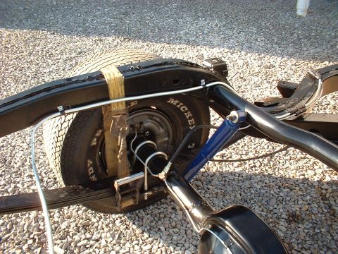 1964 Ford Galaxie - Close-up view of a vehicle's rear axle assembly, leaf springs and a blue shock absorber, with visible tire sidewall text.