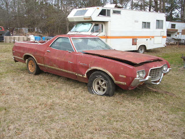 Red Ford Ranchero with a flat tire and hood open, parked in a grassy area next to an RV