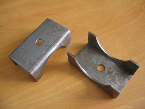 1981 Ford Bronco - Two metal brackets, likely for vehicle suspension, are shown on a wooden surface.