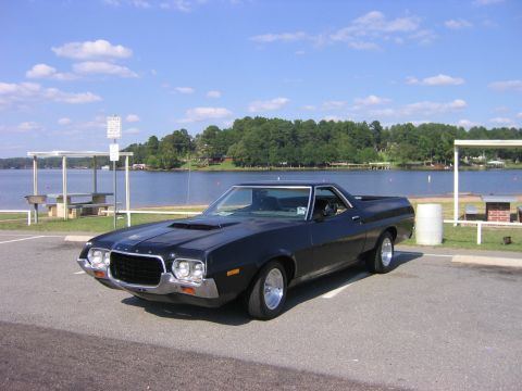 1972 Ford Ranchero - A black 1972 Ford Ranchero GT is parked in a lot next to a body of water on a sunny day.