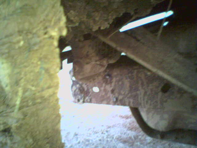 Blurry underside view of rusty vehicle frame and floor pan