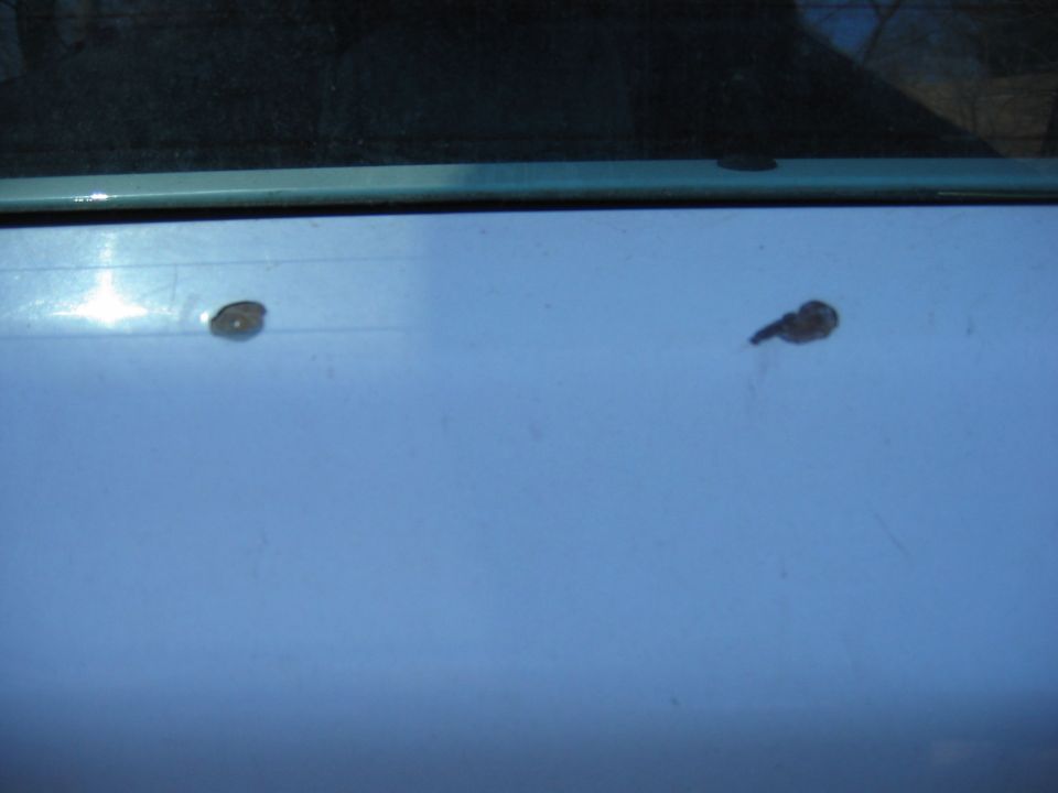 Close-up of two paint damage spots on a light-colored panel below a window on a 1995 Ford Bronco