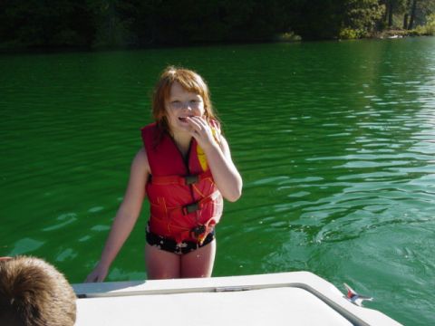1986 Ford Bronco - A young girl wearing a red life jacket stands on a boat in bright green water.