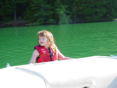 1986 Ford Bronco - A young girl wearing a life jacket smiles while on a boat in a lake surrounded by trees.