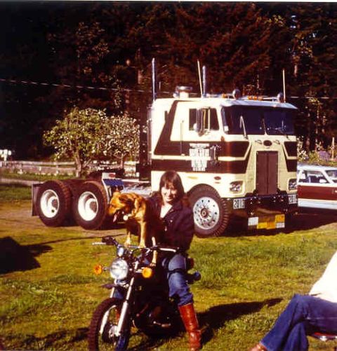 1976 Ford F-150 - A person sits on a motorcycle with a dog perched on their lap, in front of a large semi-truck.