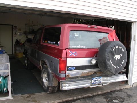 1995 Ford Bronco - Rear view of a red and silver Ford Bronco with a spare tire cover, parked inside a garage.