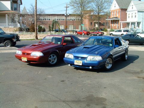 1994 Ford Bronco - Two Ford Mustangs are parked on a street in front of residential buildings.