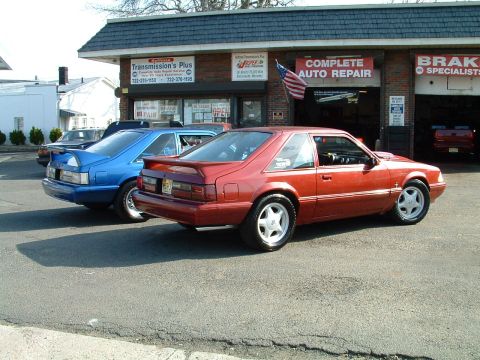 1994 Ford Bronco - Two coupes, one red and one blue, are parked in front of an auto repair shop.