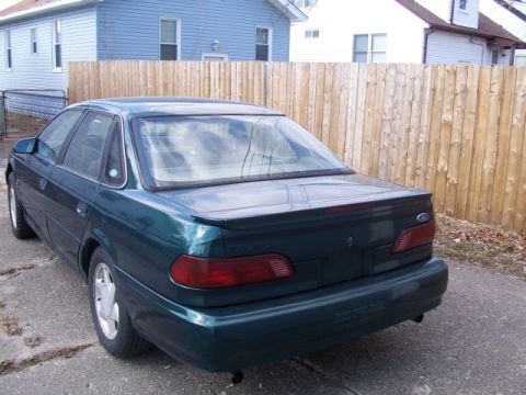 1993 Ford Taurus - The rear of a dark green sedan is shown parked outdoors with a wooden fence in the background.