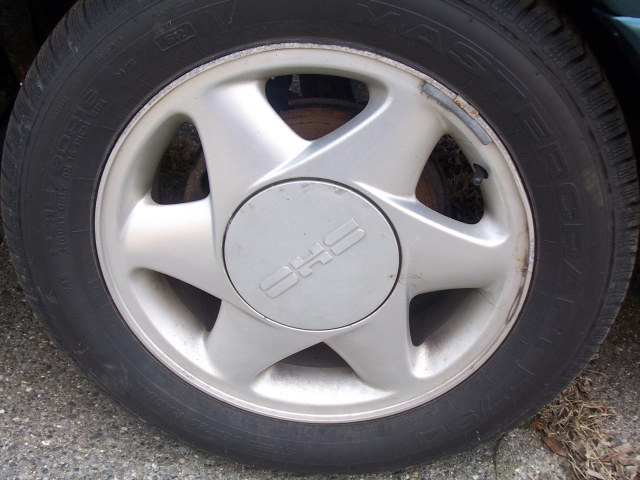 Close-up of a silver alloy wheel with a center cap displaying a stylized logo