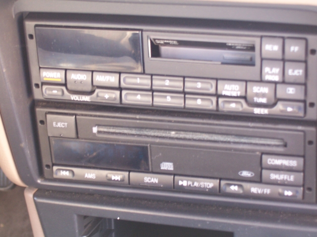 Car dashboard showing a dual-DIN radio and CD player with buttons for power, volume, AM/FM, scan, play/stop, and seek