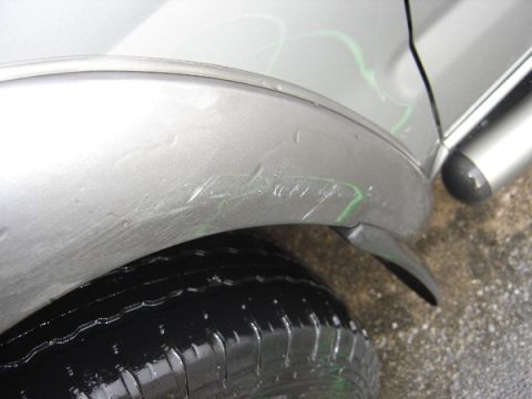1999 Ford Taurus - Scratches and green marks are visible on the silver fender of a car, near the tire.