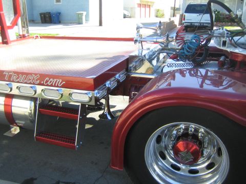 1968 Ford Mustang - Close-up of a red tow truck bed chrome accents and the text "Truck.com" visible on its side.
