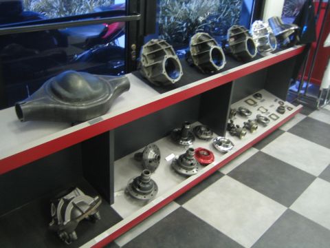 1990 Ford Bronco - Differential housings, carriers and related gear parts arranged on a black and red display shelf in a shop.