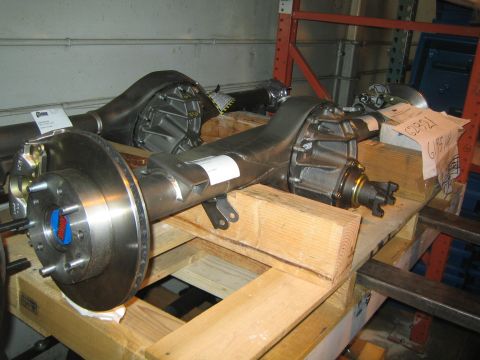 1990 Ford Bronco - polished rebuilt rear axle assembly with brake rotor and differential sits on wooden blocks on a warehouse shelf.