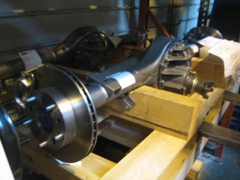 1990 Ford Bronco - bare metal axle assembly with a vented disc brake rotor and hub rests on wooden blocks in a workshop.