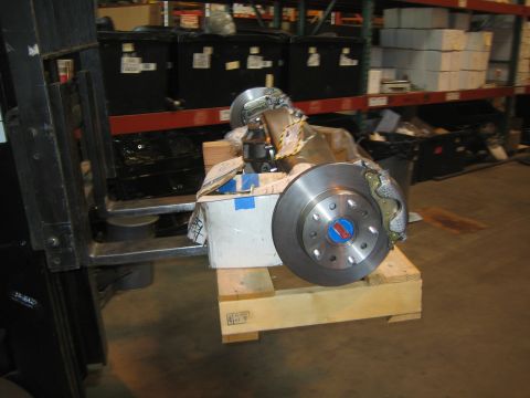 1990 Ford Bronco - axle assembly with disc brake rotor sits on a wooden pallet raised by forklift tines in a parts warehouse.