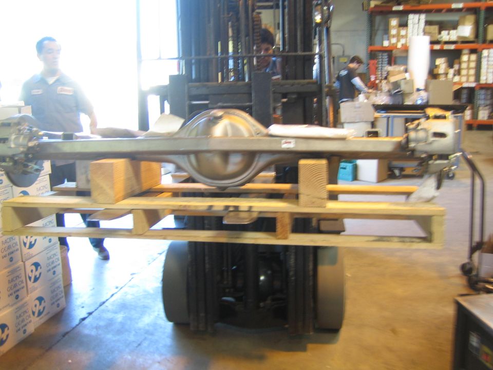 Workers and forklift carrying a large axle housing in a warehouse