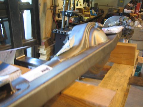 1990 Ford Bronco - long fabricated axle housing with welded center section rests on wooden blocks in a cluttered workshop.