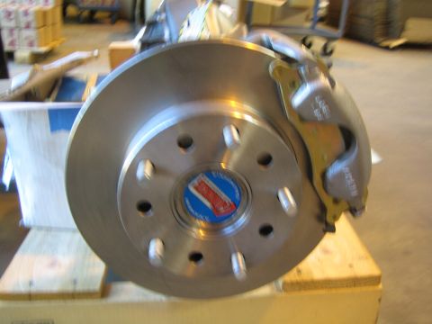 1990 Ford Bronco - Close-up of a vented disc brake rotor and caliper mounted on an axle hub with a blue and white center sticker.