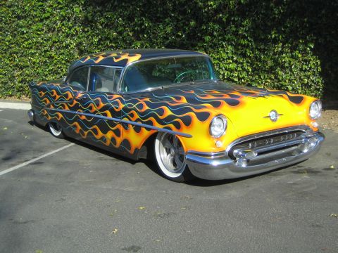 1968 Ford Mustang - A customized 1955 Oldsmobile with a vibrant flame paint job is parked outdoors.