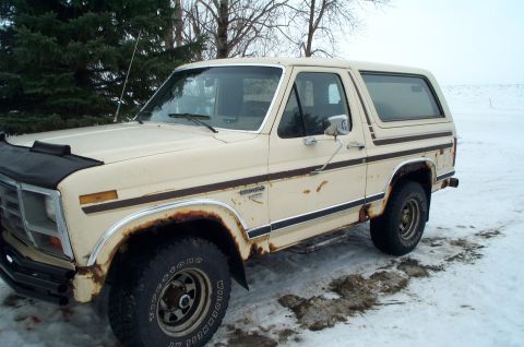 1984 Ford Bronco - This 1980s Ford Bronco shows significant rust and wear, with its distinctive brown side trim visible.