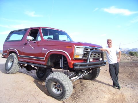 1984 Ford Bronco - A man poses with his lifted red Ford Bronco in a dry, outdoor landscape under a blue sky.