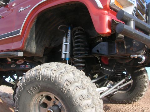 1984 Ford Bronco - Close-up of the modified suspension and large tires on a red 1984 Ford Bronco.