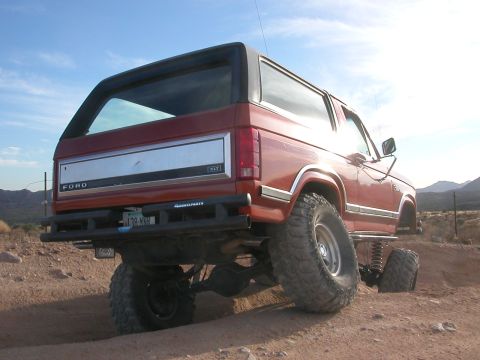 1984 Ford Bronco - This lifted Ford Bronco is navigating rough terrain on a sunny day.