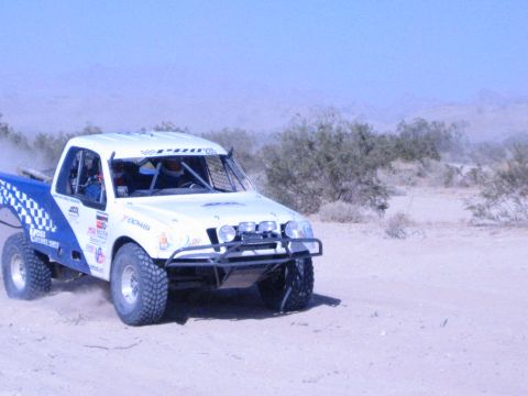 White and blue off-road race truck with roll cage driving through desert sand