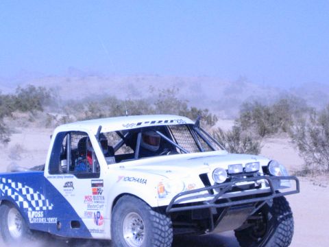 White and blue desert race truck with sponsor decals seen from the side in motion