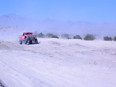 Red off-road race truck cresting a sandy berm with mountains in the background
