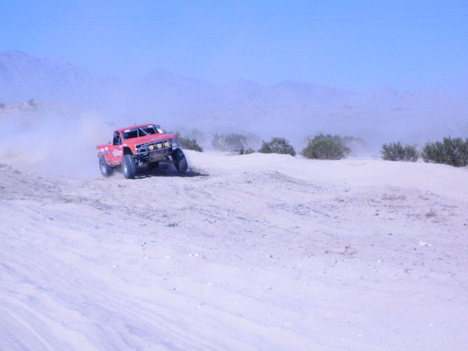Red off-road race truck driving over sandy desert terrain throwing up dust