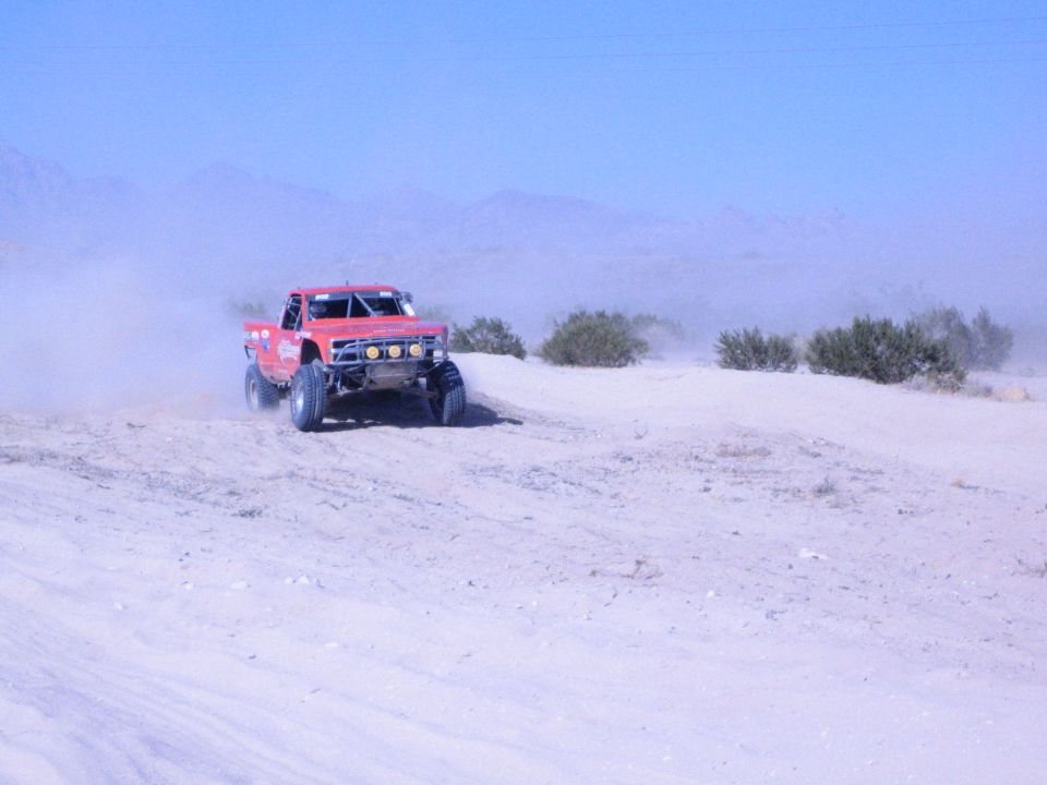 Red off-road race truck with light bar driving across open desert sand