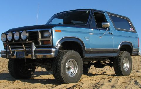 1984 Ford Bronco - This 1984 Ford Bronco features a two-tone paint scheme and auxiliary lighting, captured in a three-quarter front view.