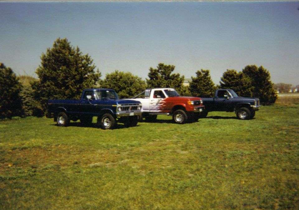 Three pickup trucks parked in a grassy field under a clear blue sky