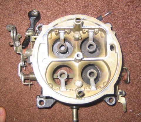 1969 Ford Mustang - A carburetor with four barrels and visible linkage is shown against a brown, carpet-like background.