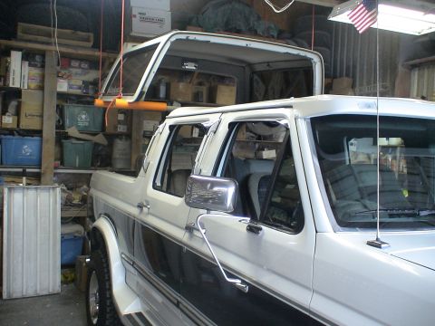 1993 Ford C-350 (Centurion Conversions) - The removable roof of a white Ford Bronco is hoisted above the vehicle in a cluttered garage.